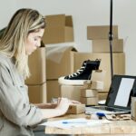 A woman packing boxes for her online store, surrounded by packaging materials and a laptop.