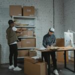 Two workers handling packages and organizing stock in a warehouse setting.
